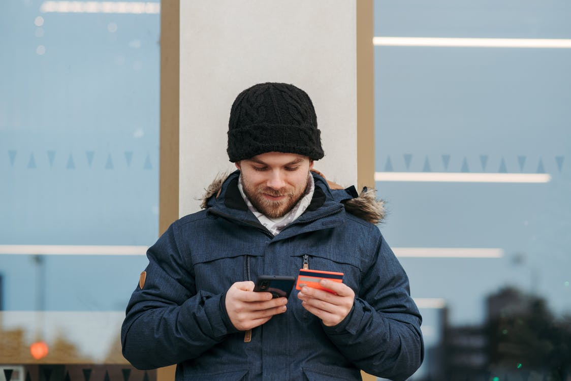 Cheerful man adding his credit card details to his smartphone  