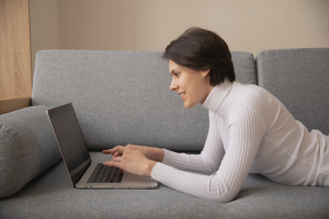 Woman smiling while comfortably using her laptop on the sofa
