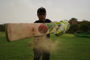 Mid-action shot of a cricket player hitting a red Kookaburra ball with his bat