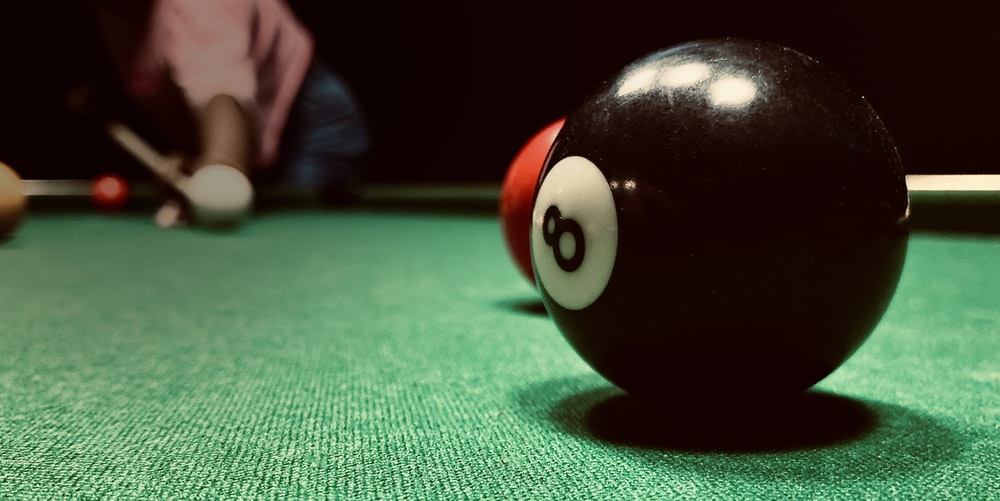 A player aiming at a black ball on a green pool table