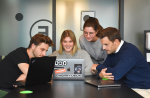 Four young people sitting on an office table with their laptops