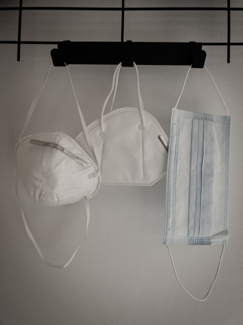 Three white color face masks hanging off a wall hook