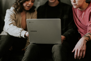 Three people browsing on a Samsung laptop on the middle person’s lap