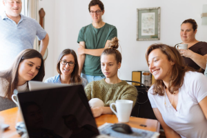 A group of people around a table looking and smiling at a laptop screen