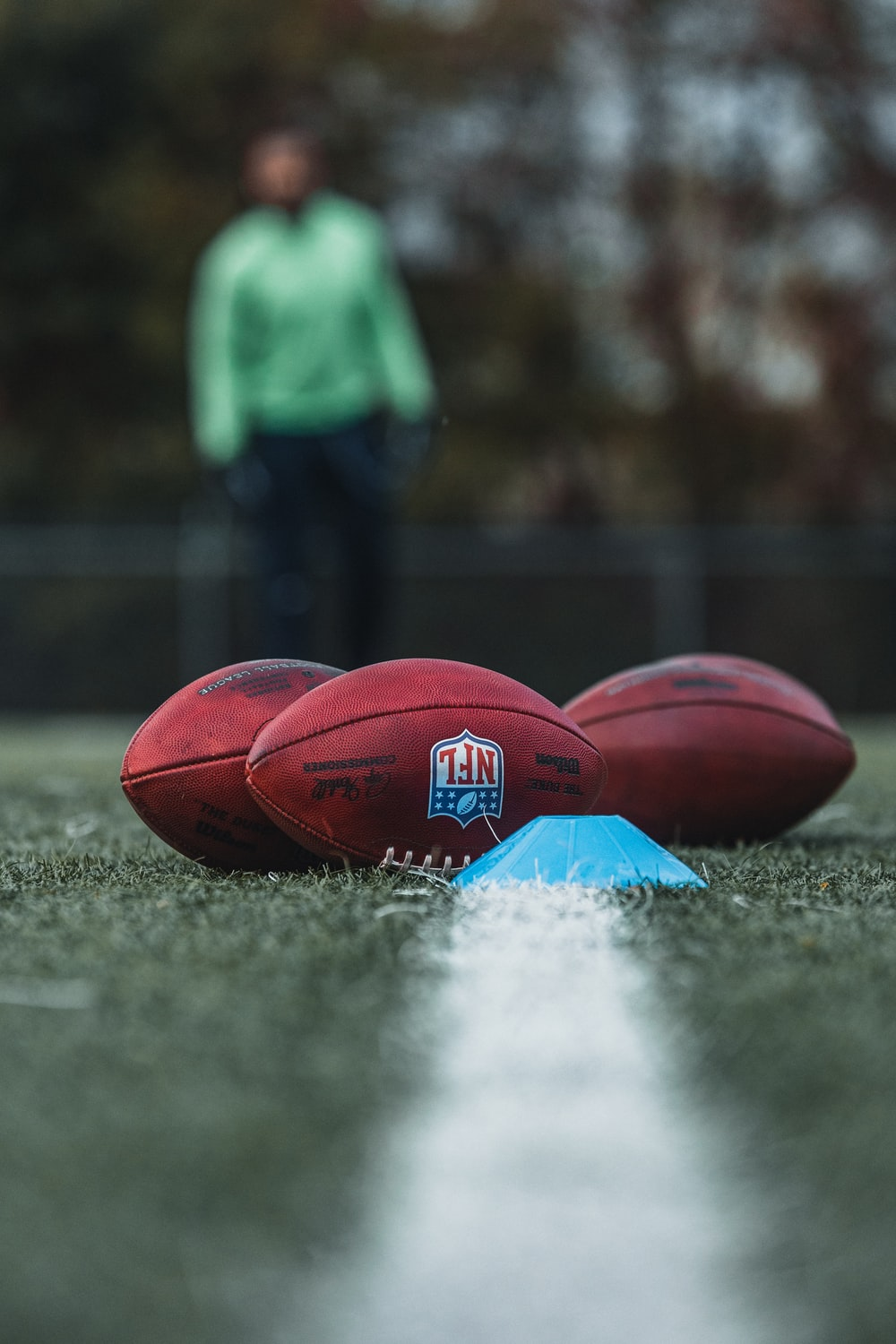 Three brown NFL labeled footballs on the ground