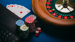 Poker chips on a laptop with cards and a roulette wheel beside them