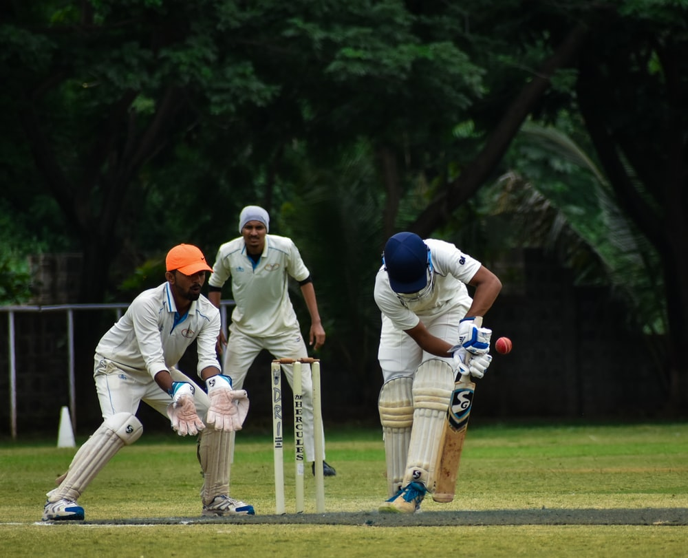 Two cricket fielders in position behind the wicket with a batsman hitting a ball