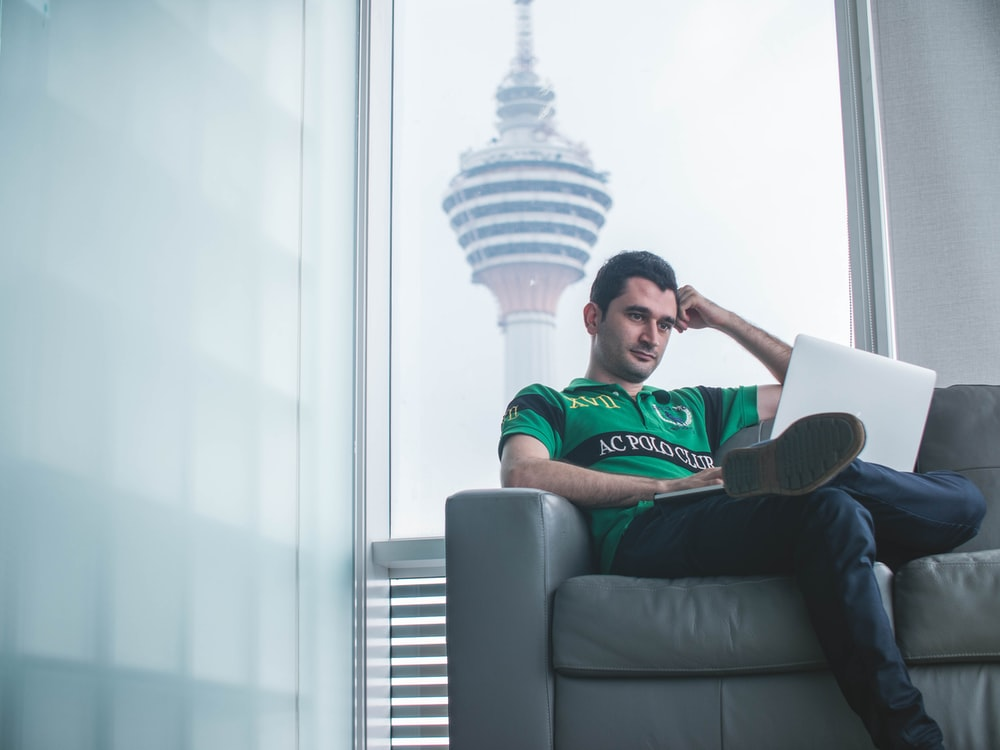 Man sitting on a couch in a relaxed position and using the laptop in his lap