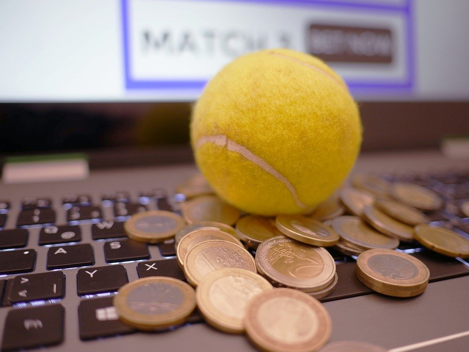 Close up of a tennis ball resting on top of some coins on a laptop keyboard