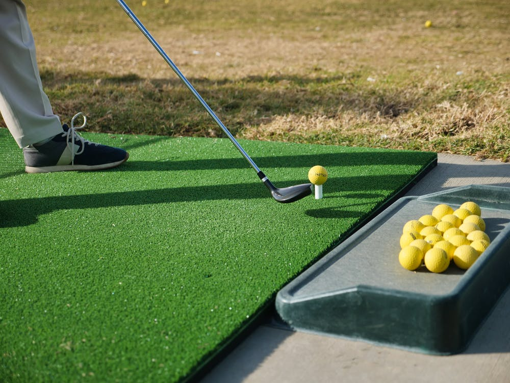 A golfer placing their club against a golf ball on a tee on a field