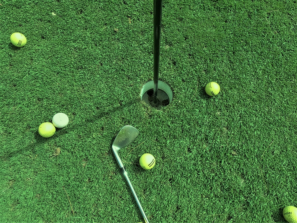 A golf club lying on the grass next to a cup and some balls