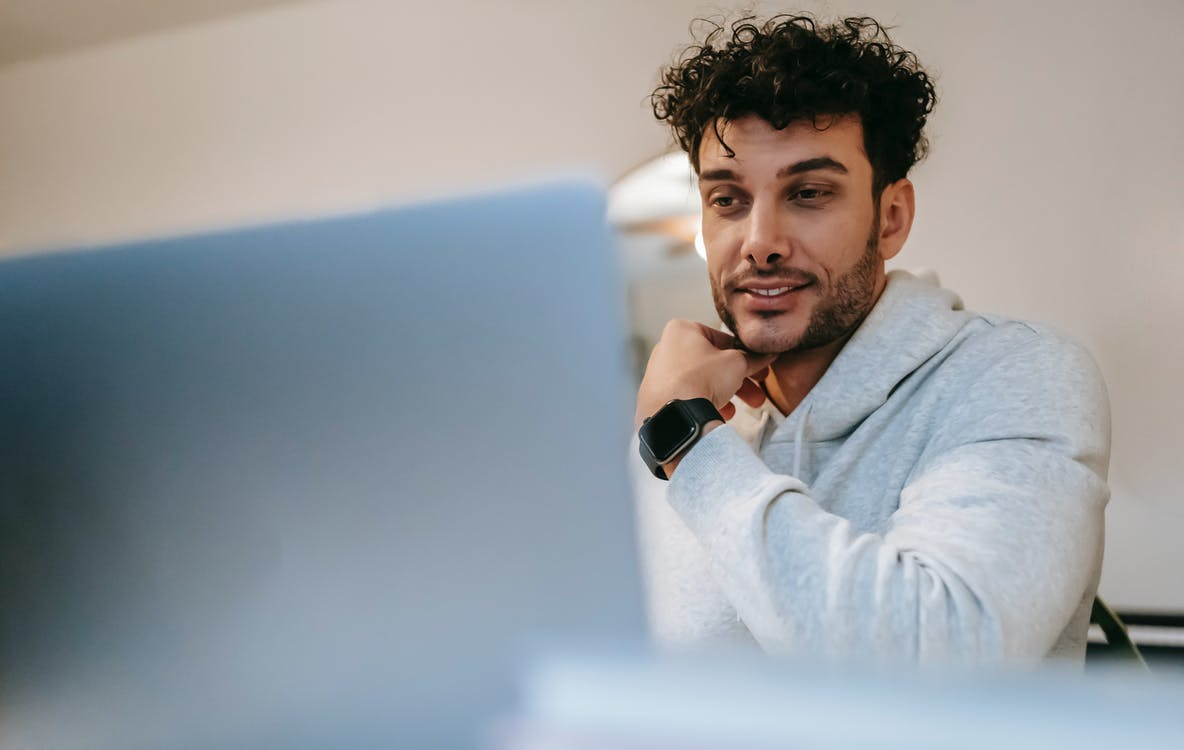 A man with curly hair smiling at his laptop screen