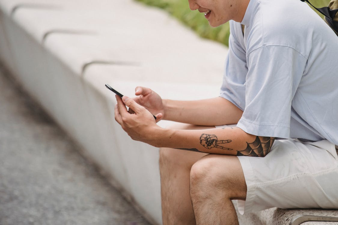 A man sitting at the side of the road and smiling at his phone