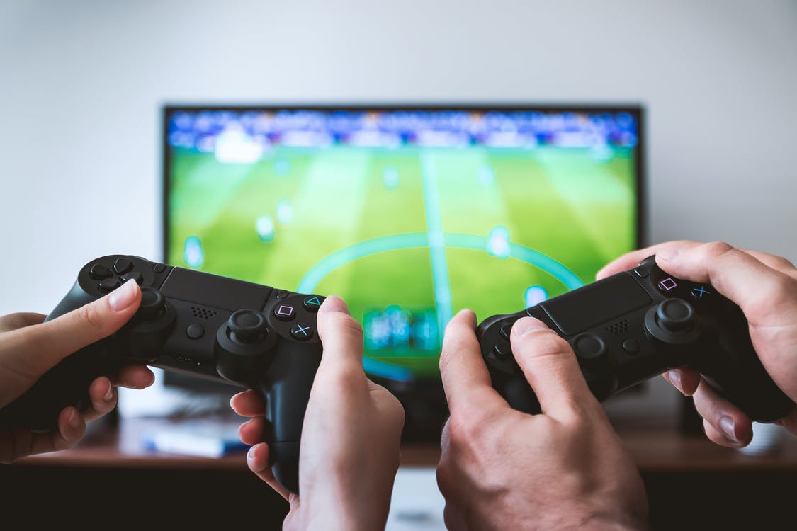 Two people holding controllers in front of a TV screen displaying a football match