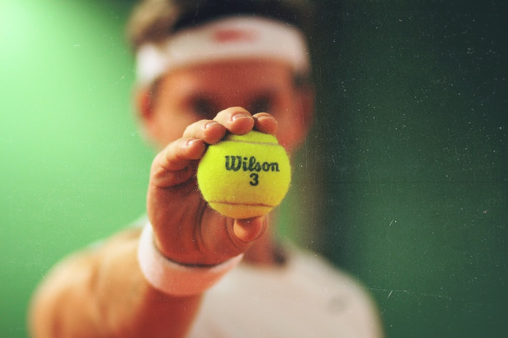 A tennis player holding a Wilson 3 tennis ball up to the camera