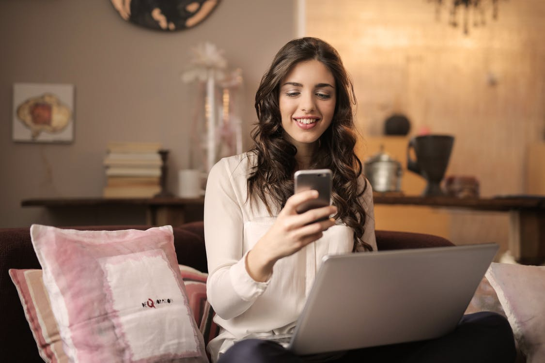 A woman smiling while using her phone and laptop