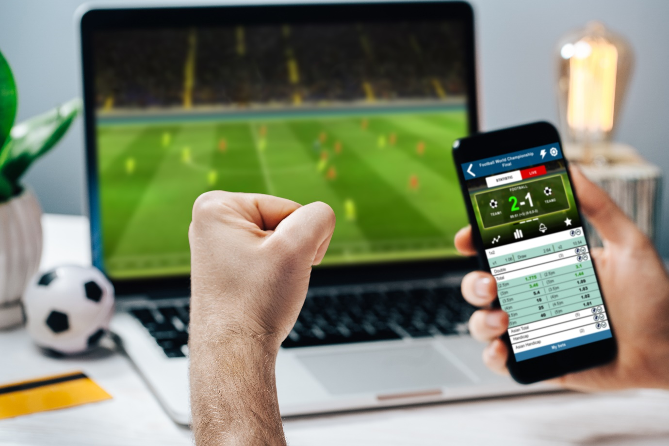 Person watching football on the laptop while betting on a smartphone