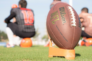 A Wilson NFL ball on the grass with players sitting in the background