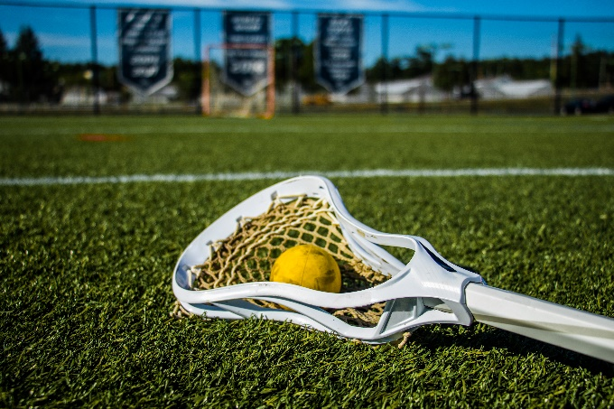A yellow lacrosse ball and white stick on a grassy field