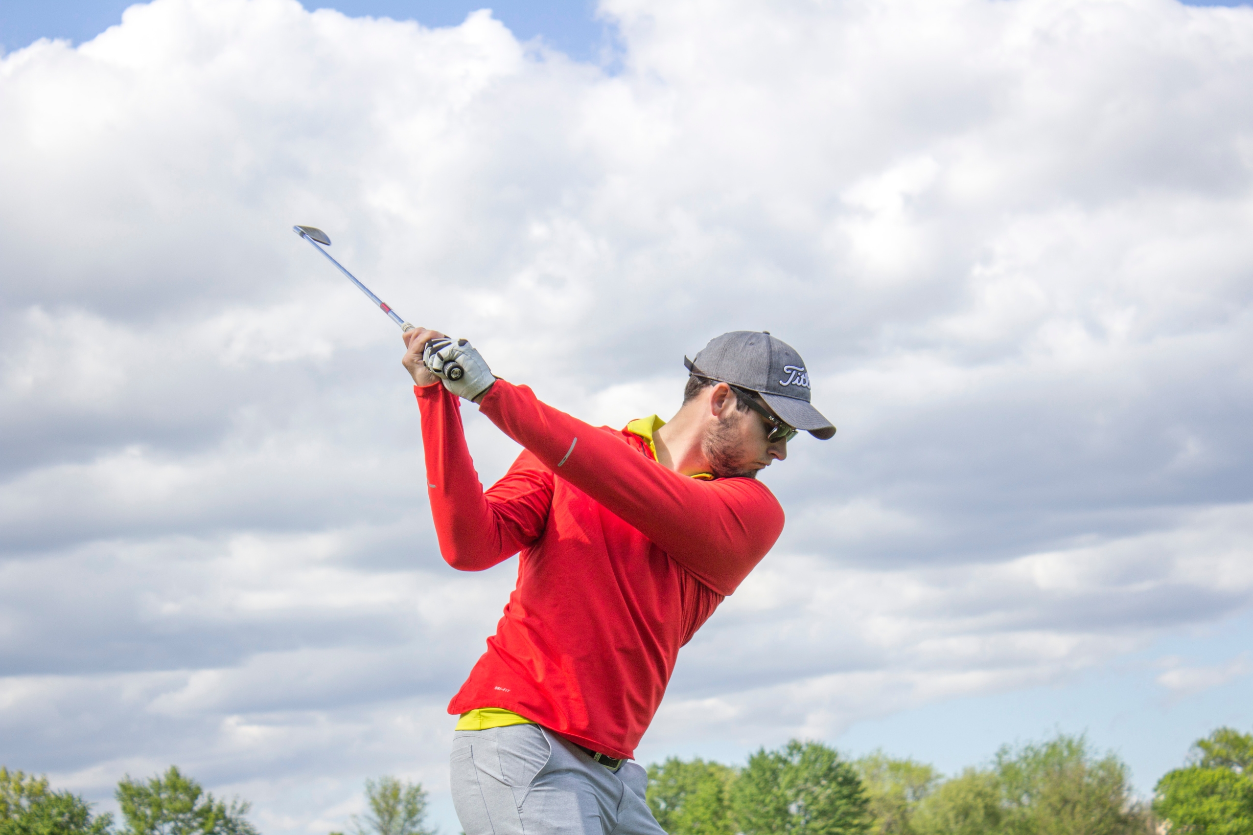 A golfer wearing a hat swinging a golf club