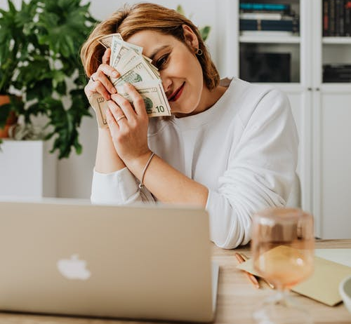 Woman holding cash while looking at the laptop 