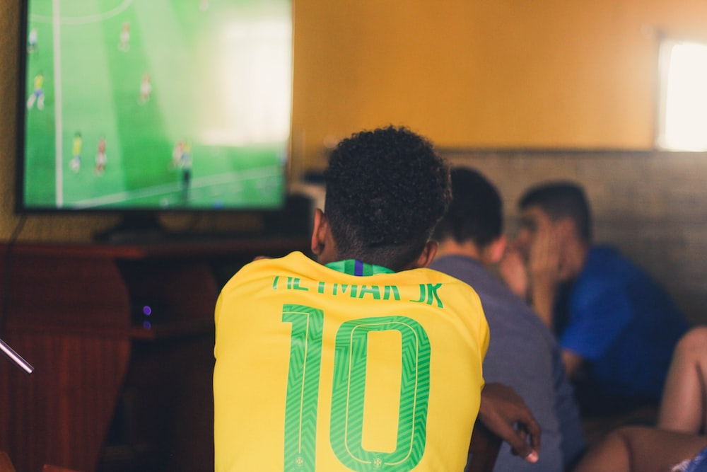 A man wearing a Brazil jerseywatching a soccer game on TV